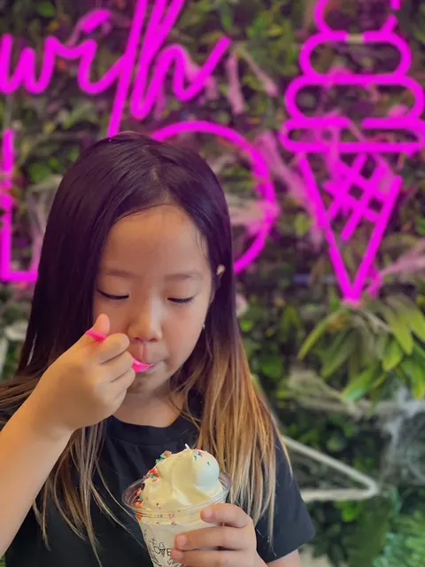 A child eating a taiyaki in front of the shop's neon sign.