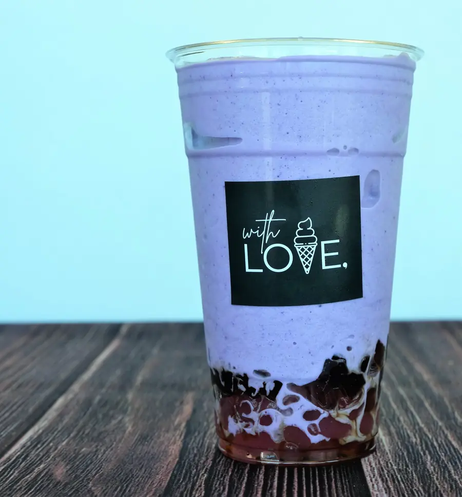 A tall taro smoothie with black boba, on a wooden table.