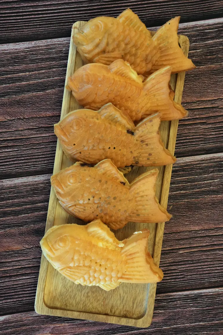 A row of golden taiyaki, fish-shaped waffle cakes, lined up on a wooden board.